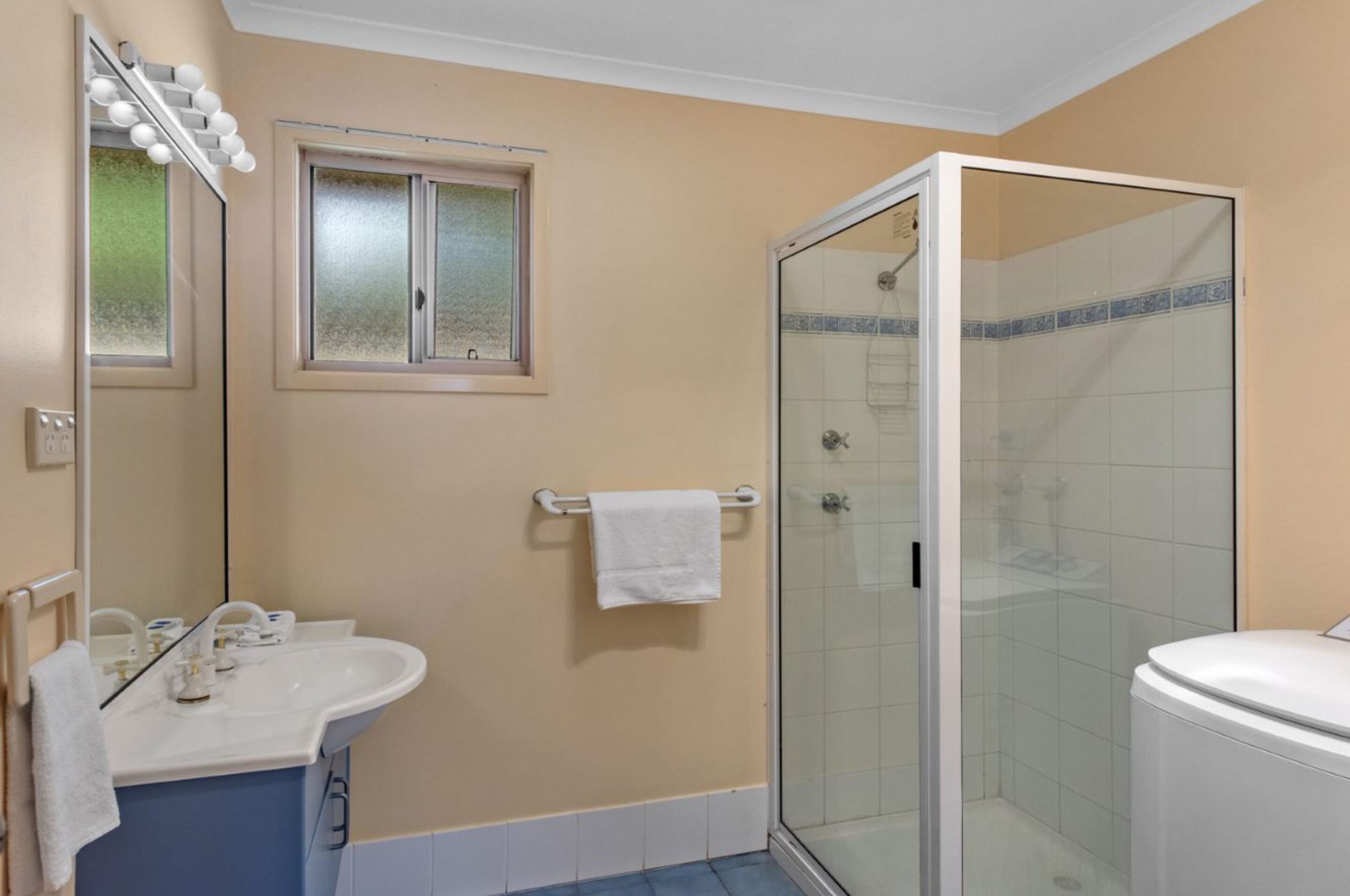 A bathroom with a glass-enclosed shower, a sink with a mirror, and a window with frosted glass.