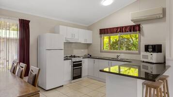 A modern kitchen with white cabinets, a gas stove, an oven, a microwave, and a window with a view of greenery.