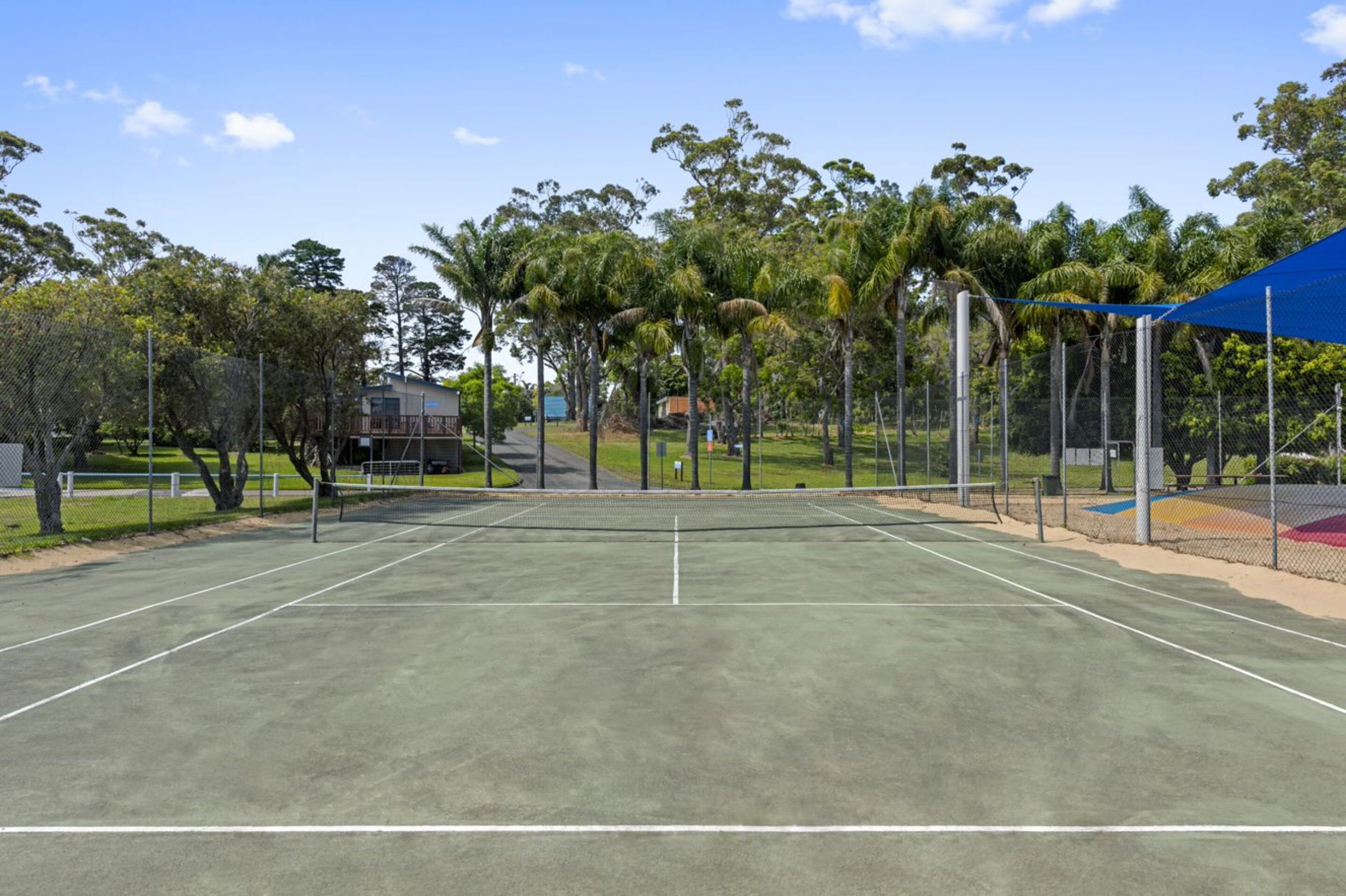 Una cancha de tenis con red, rodeada de árboles y una valla.