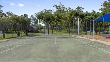 Una cancha de tenis con red, rodeada de árboles y una valla.