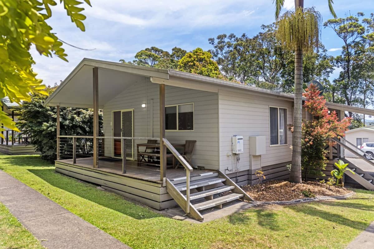 Einbungalow mit überdachter Veranda, einer kleinen Terrasse und einer Treppe zum Eingang.