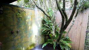 Una terraza de madera con una fuente de agua, rodeada por una valla de madera y abundante vegetación.