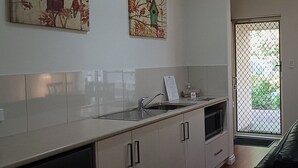 Una cocina con un lavamanos de acero inoxidable, armarios blancos y vistas a un espacio exterior por una puerta de cristal.