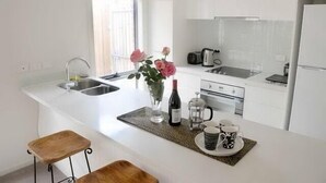 Een moderne keuken met witte kastjes, een inbouwgootsteen, een koffiezetapparaat en een wijnfles op het aanrecht.