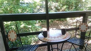 Een overdekt terras met een tafel betegeld met mozaïek en metalen stoelen, omringd door groen.