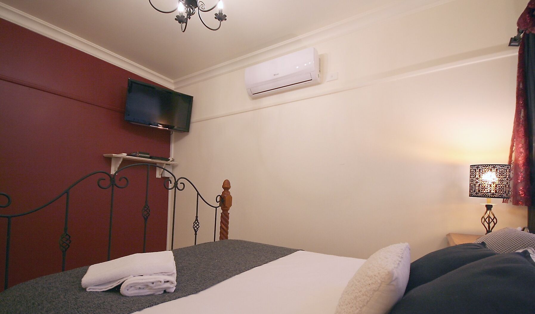 A hotel room with a bed, a TV mounted on the wall, an air conditioner, and a bedside lamp.