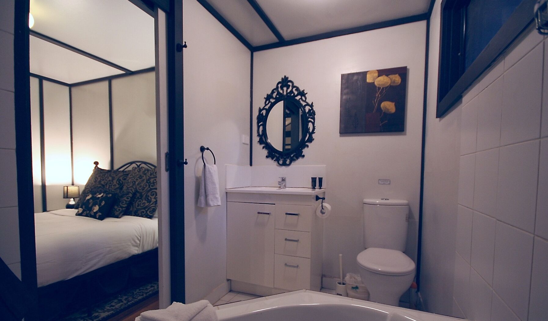 Un dormitorio con cama, mesita de noche y tocador. Cuenta con un baño que incluye lavabo, espejo, inodoro y bañera.