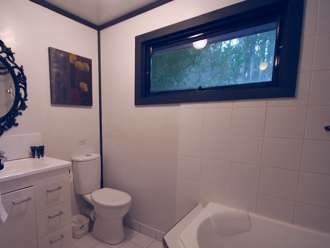 Ein Badezimmer mit Toilette, Badewanne, Fenster, Waschbecken und Spiegel.