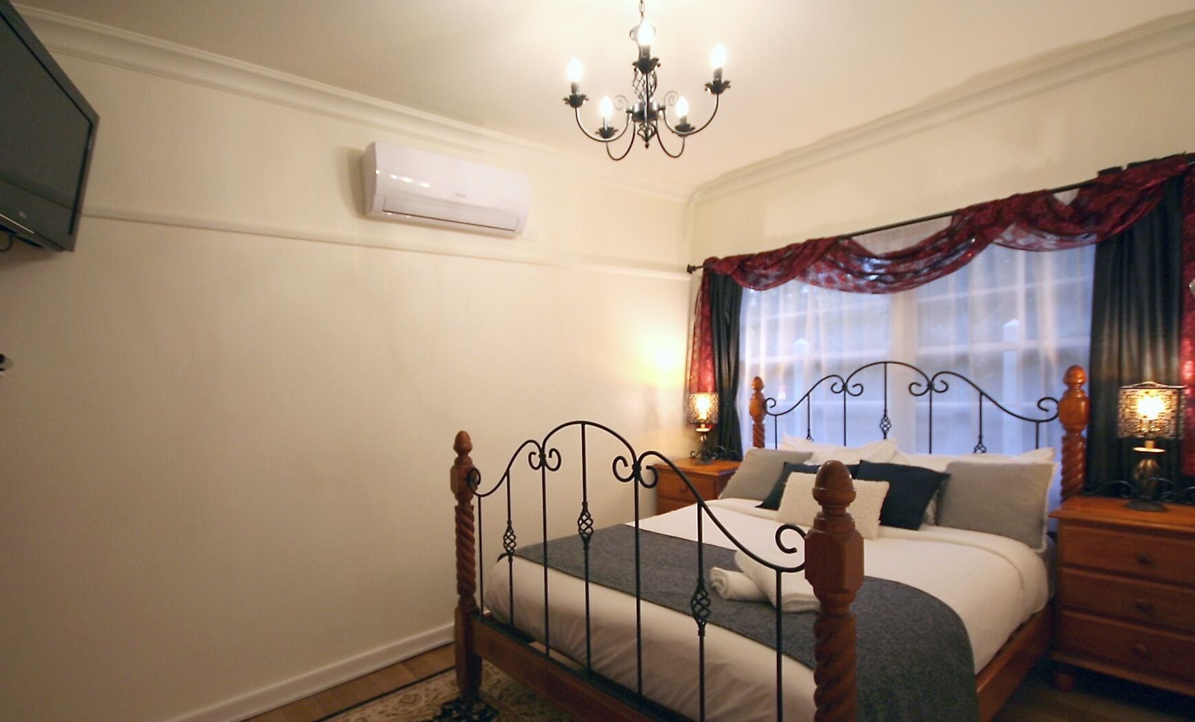Un dormitorio con cama con dosel, candelabro, aire acondicionado y ventana con cortinas.