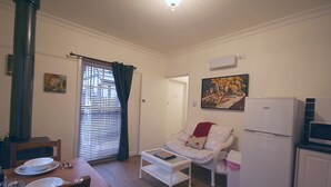 Een compacte woonruimte met een eethoek, een bank, een koelkast en een schilderij aan de muur.