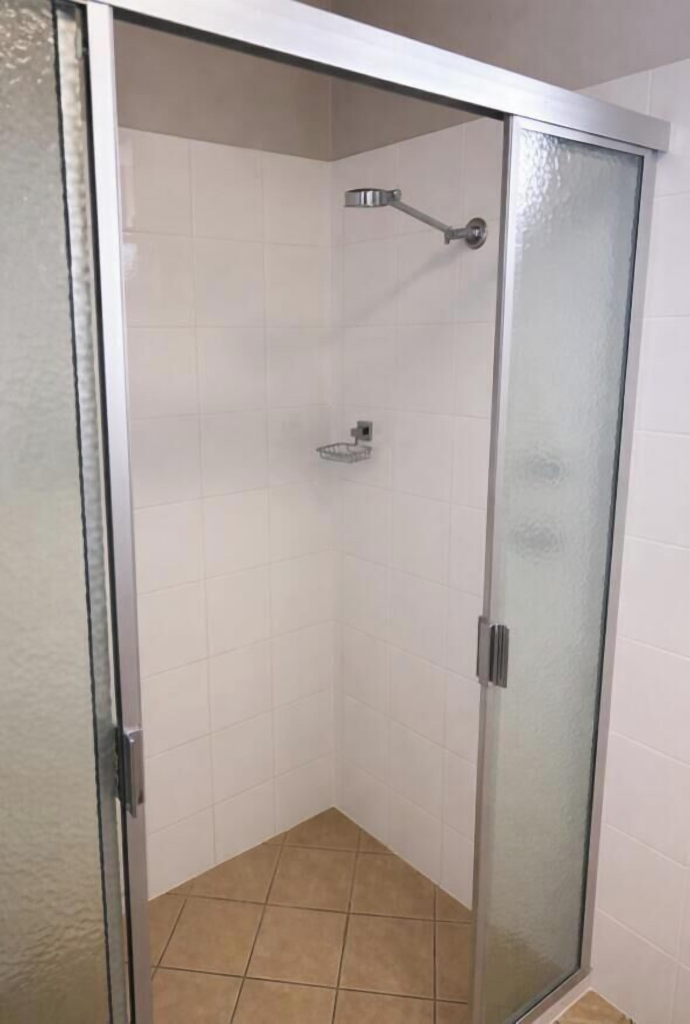 A glass-enclosed shower with a handheld showerhead and a wall-mounted faucet.