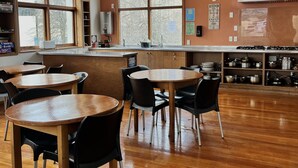 A spacious dining area with wooden tables and chairs, a kitchen area with stainless steel appliances, and large windows providing natural light. - On Top Apartments & Hostel Backpackers (Dunedin)