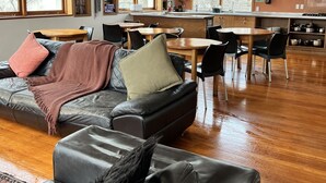 A modern living room with a leather sofa, wooden dining table, and kitchen area. - On Top Apartments & Hostel Backpackers (Dunedin)