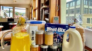 A kitchen counter with a pitcher of yellow liquid, jars of condiments, a carton of milk, and a box of Weet-Bix cereal. - On Top Apartments & Hostel Backpackers (Dunedin)