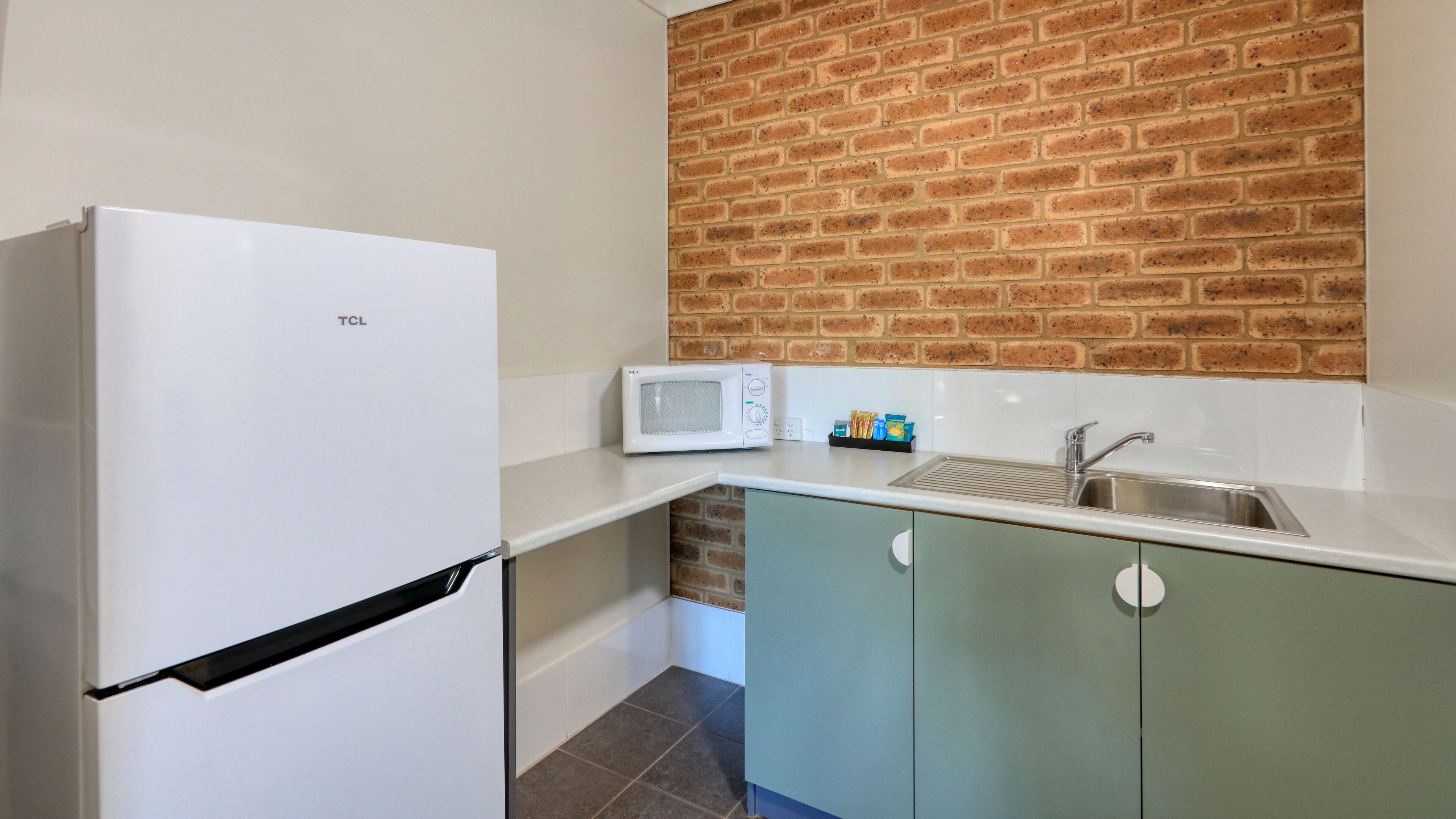 A compact kitchen with a white refrigerator, a microwave, a sink, and light green cabinets.