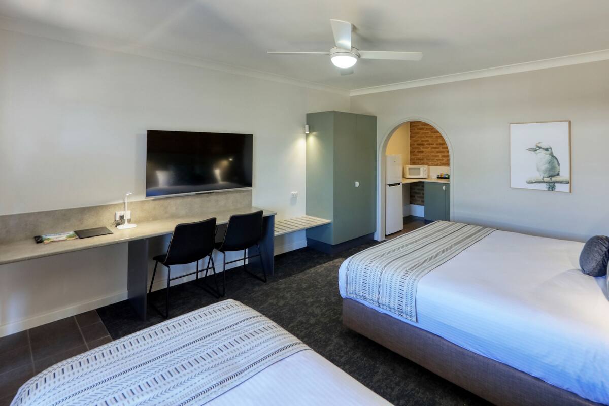 A hotel room with two beds, a desk with a flat-screen TV, a seating area with chairs, a microwave, and a small kitchenette.