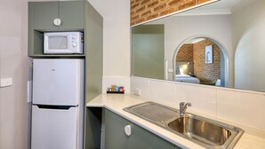 Una kitchenette compacta con un refrigerador blanco, un microondas y un lavamanos de acero inoxidable.