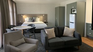 Una habitación de hotel moderna con cama, sofá, mesa de comedor y kitchenette.
