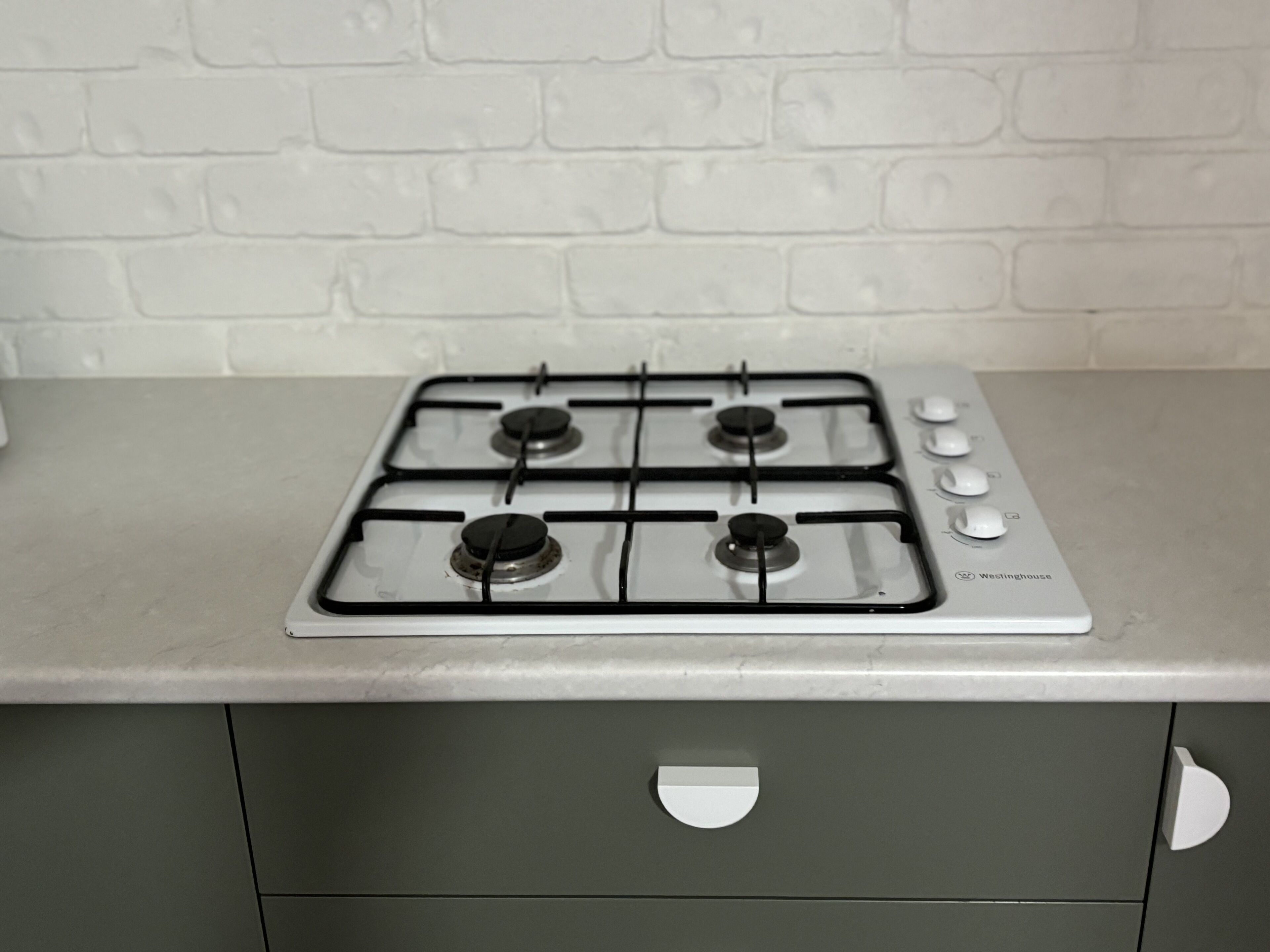 A kitchen with a gas stove, a white brick wall, and a grey cabinet.