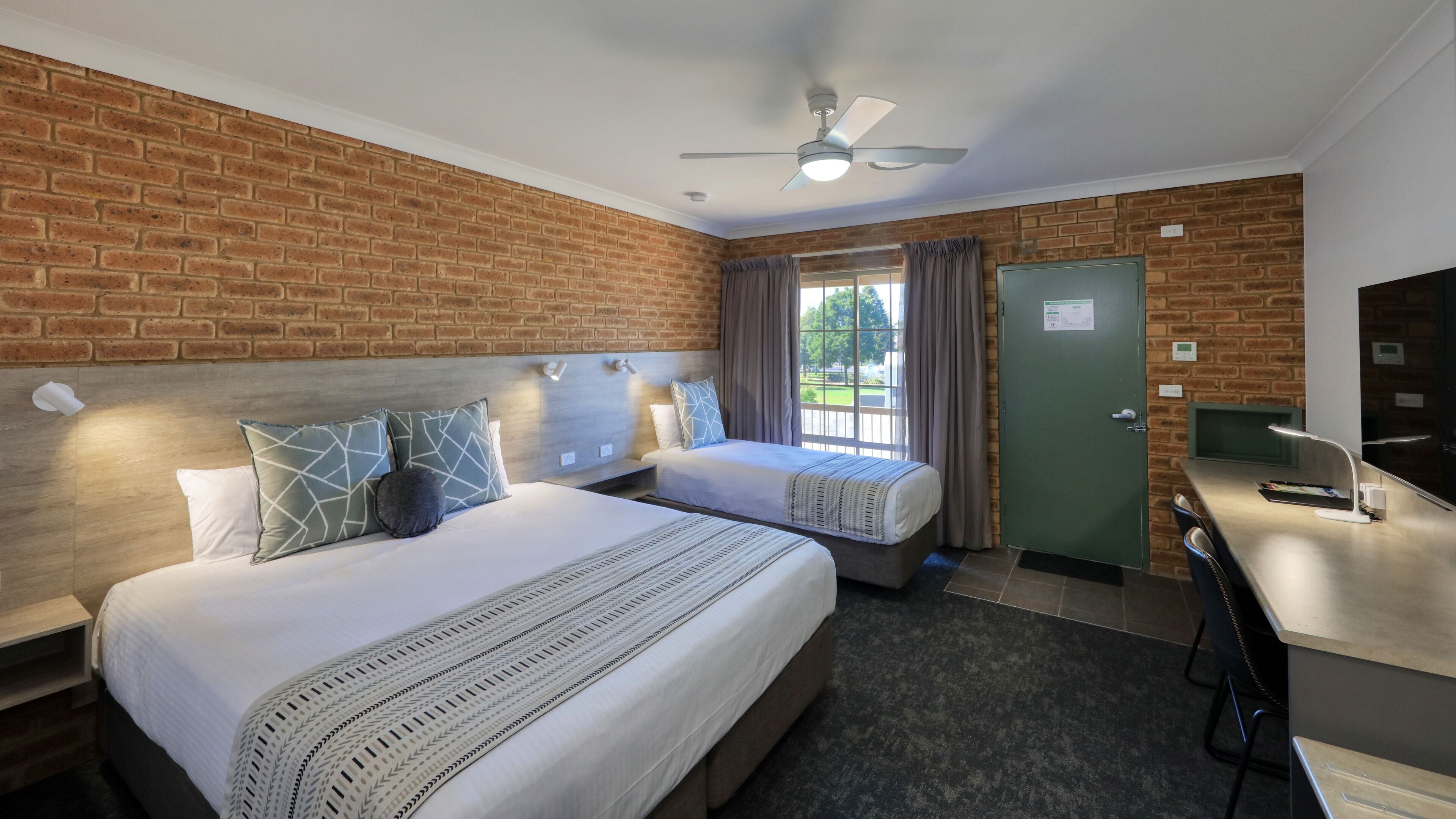 A hotel room with two beds, a desk, a TV, and a green door.
