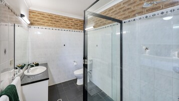 Un baño moderno con cabina de ducha de vidrio, un lavamanos blanco y un inodoro.