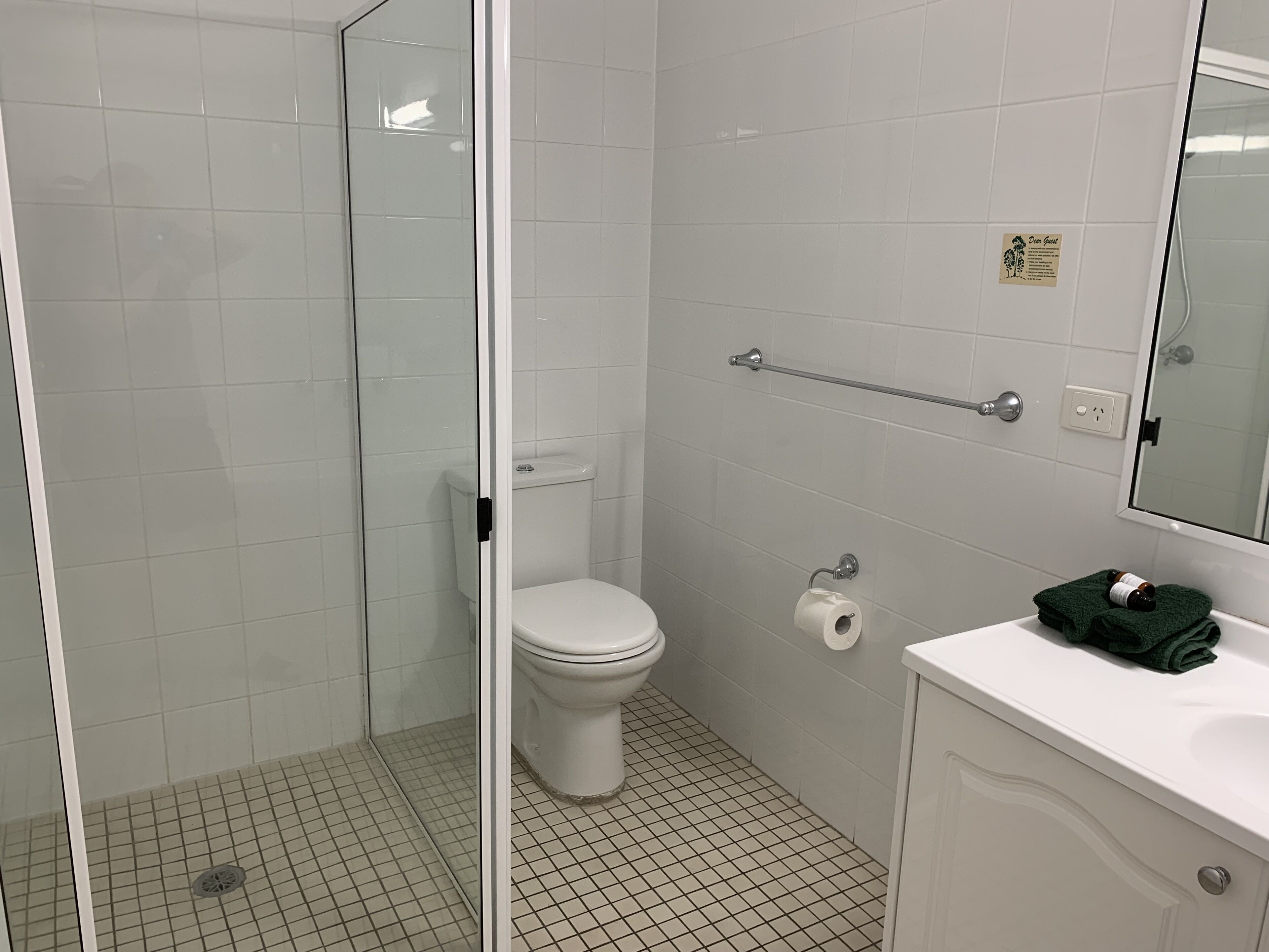 A bathroom with a toilet, a glass shower enclosure, a towel rack, and a sink with a mirror.
