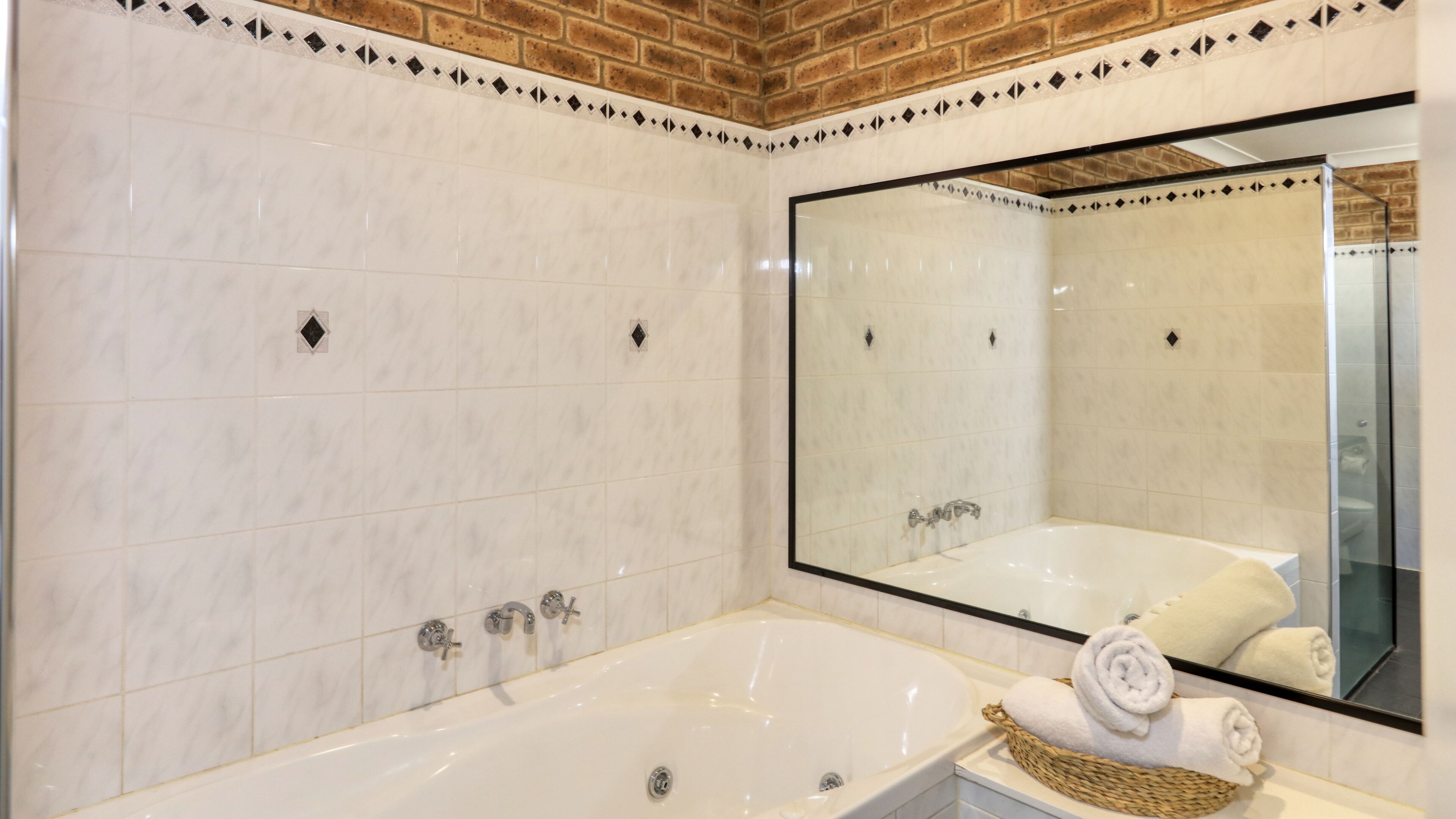 Un baño moderno con un espejo grande, una bañera y un cesto para toallas.