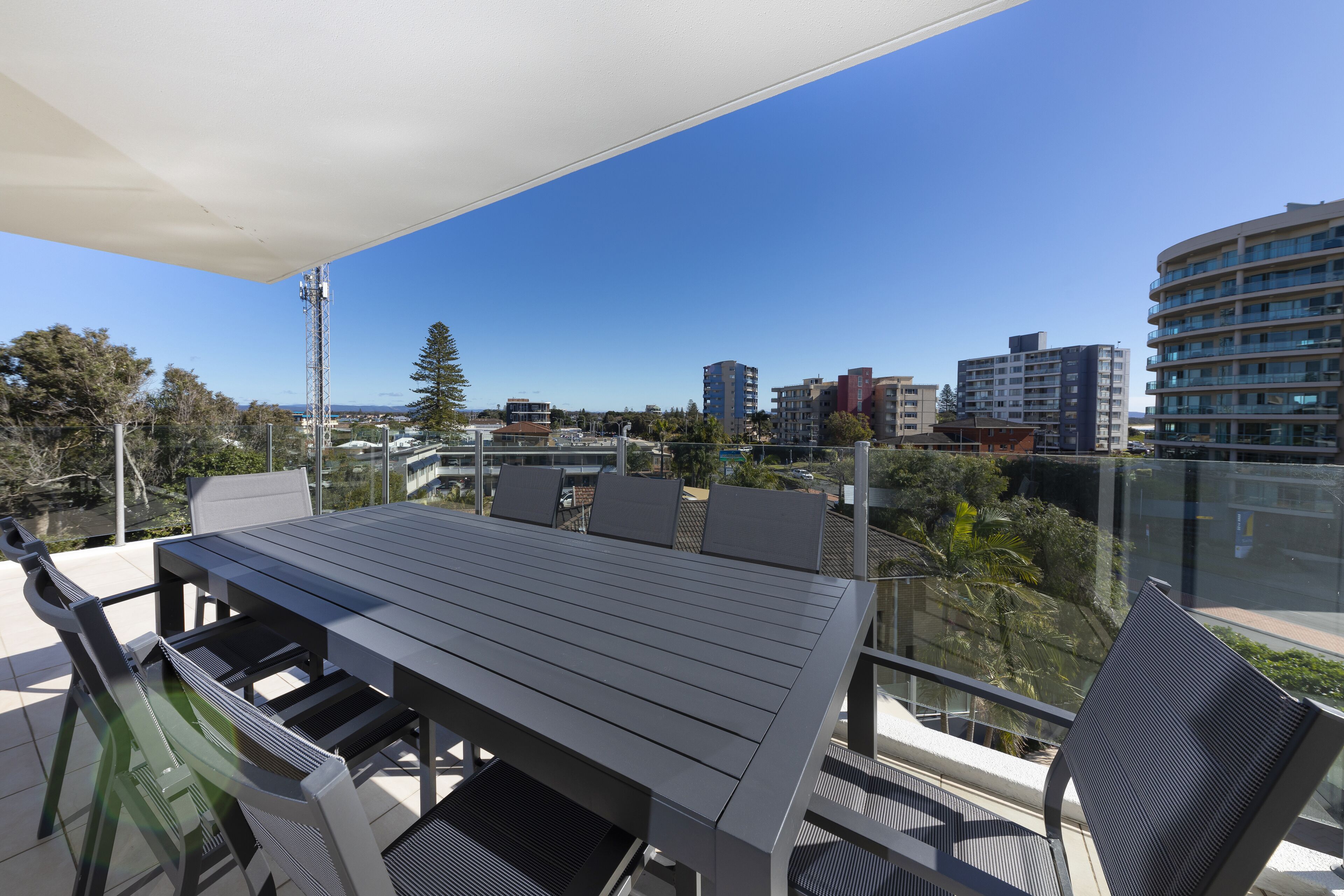 A balcony with a table and chairs, overlooking a cityscape with buildings and trees.