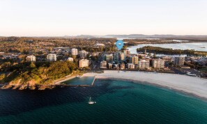 An aerial view of a coastal city with dense residential buildings, a beach, and a marina. - Sevan Apartments (Forster)
