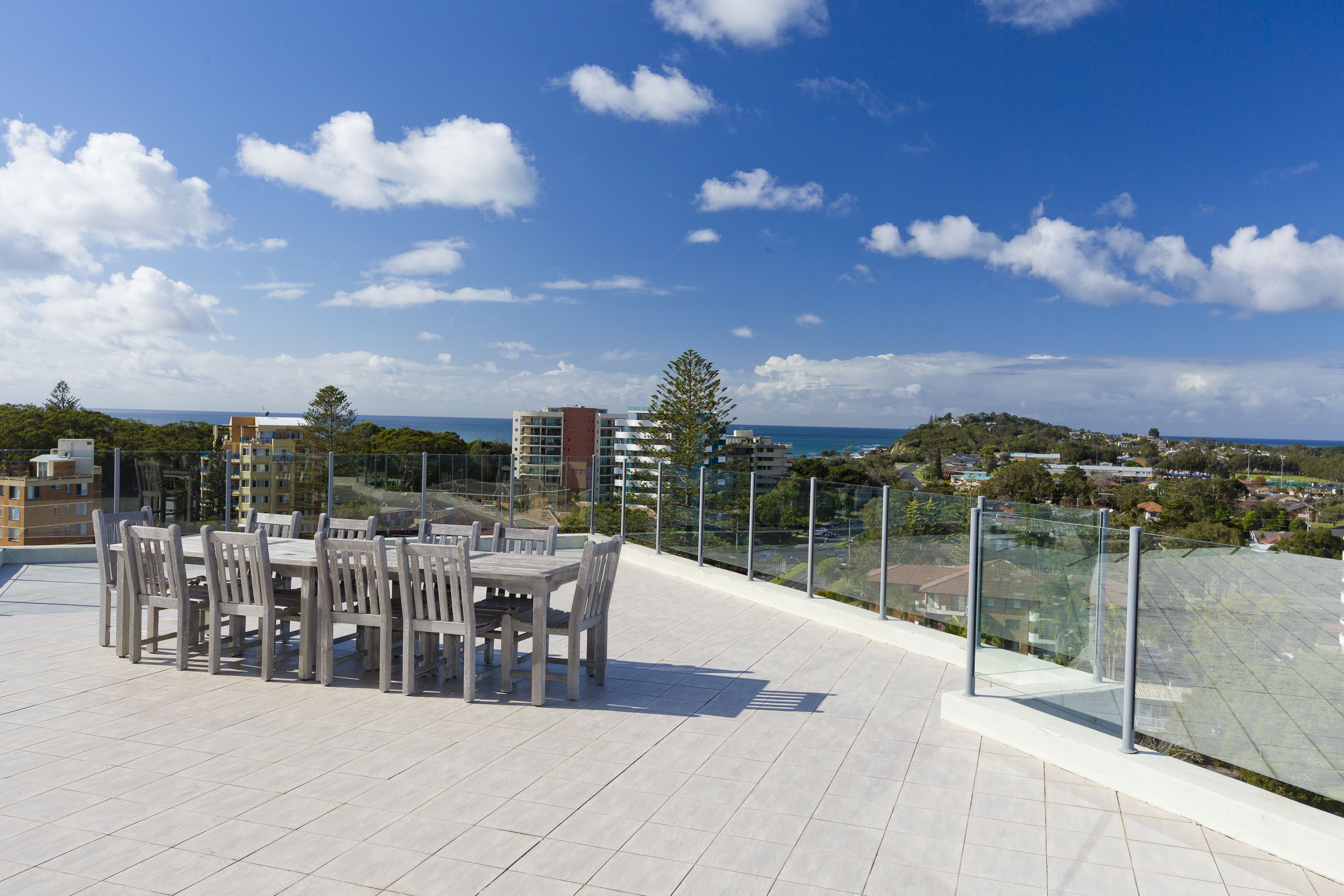 Una terraza en la azotea con una mesa y sillas, con vistas a una ciudad costera con edificios y áreas verdes.