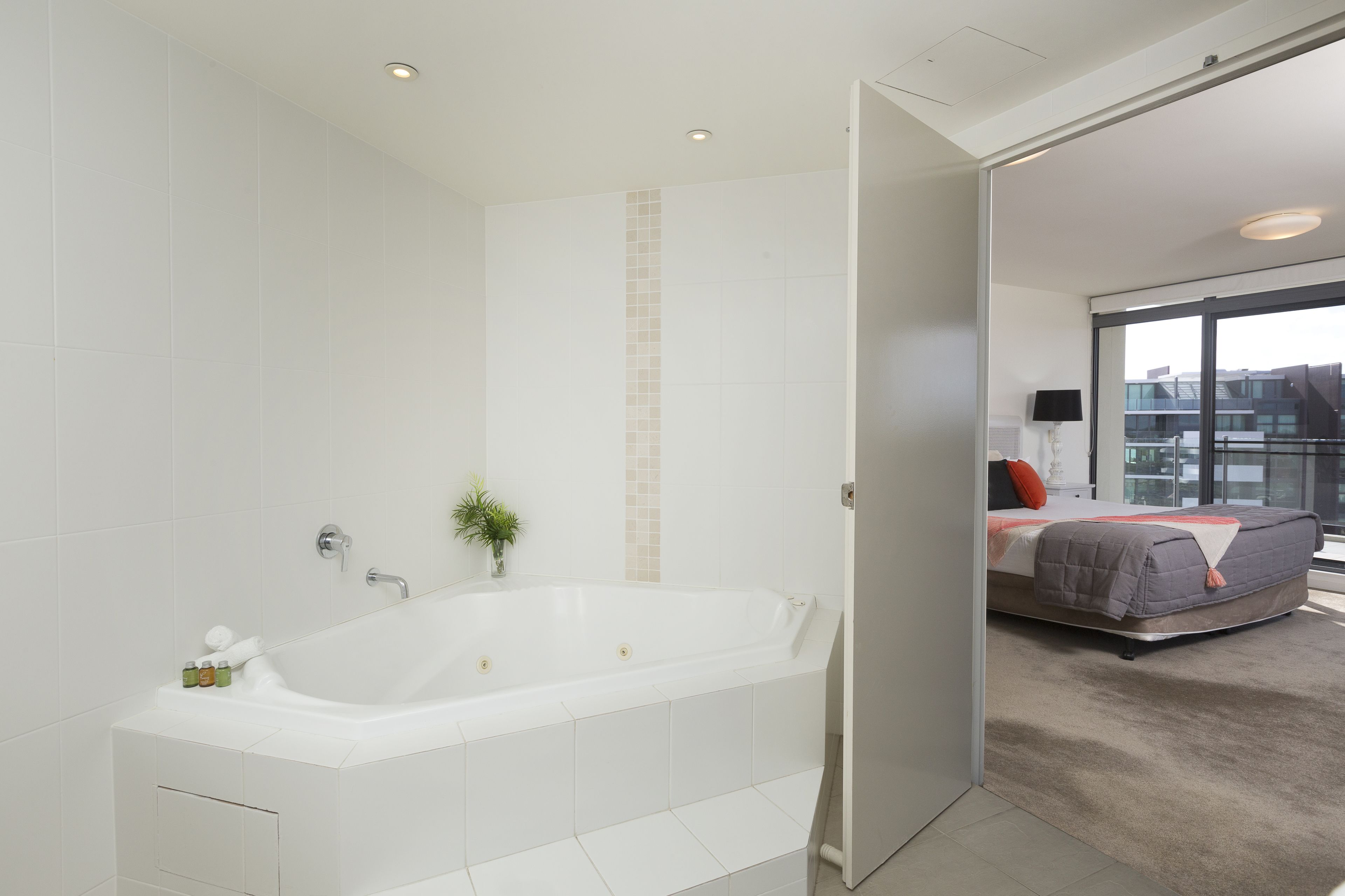 Ein modernes Badezimmer mit einer großen Badewanne, einer kleinen Pflanze und einem Spiegel.