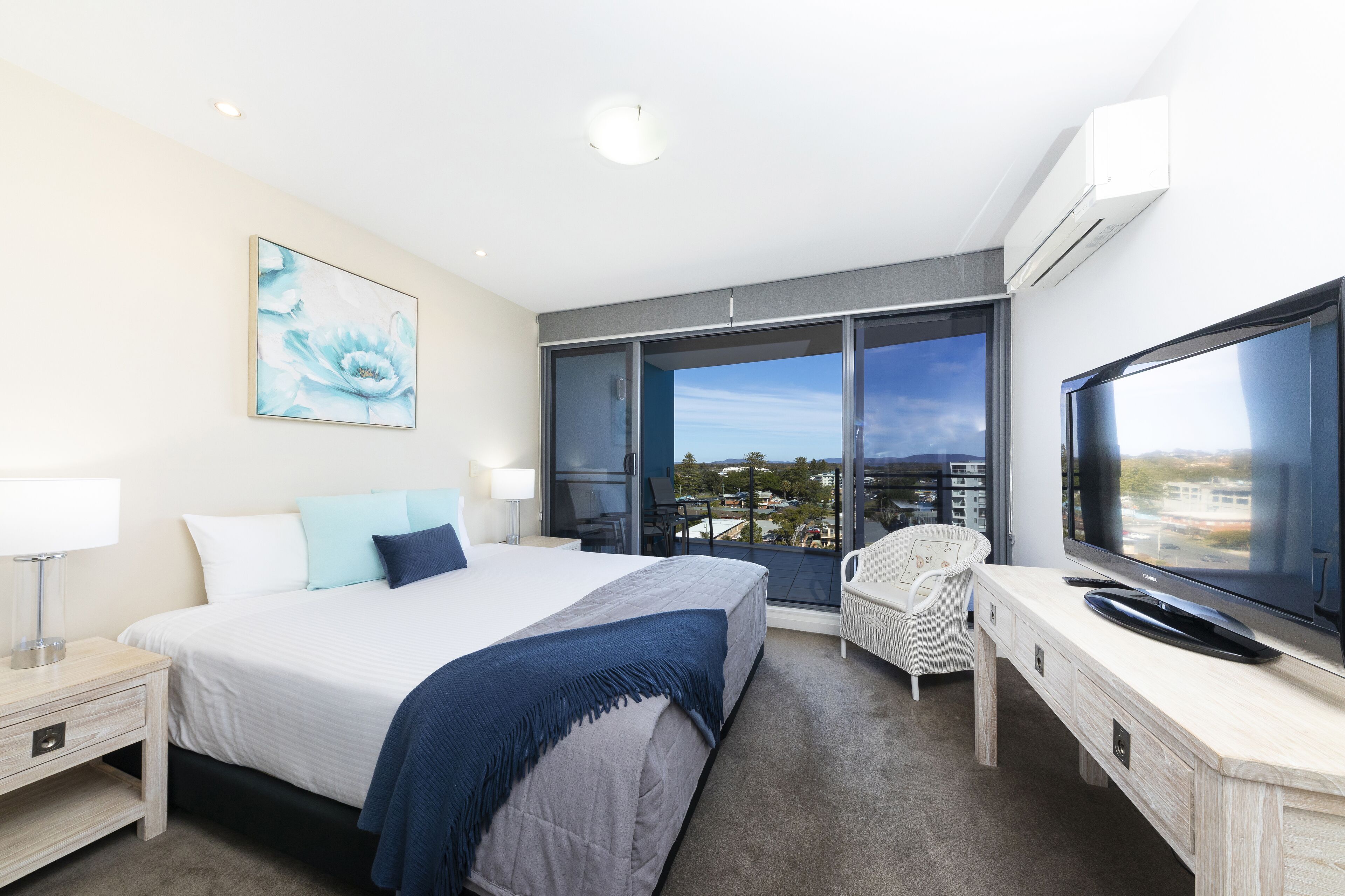 A modern hotel room with a large bed, a flat-screen TV, a balcony with a view, and a desk with a chair.