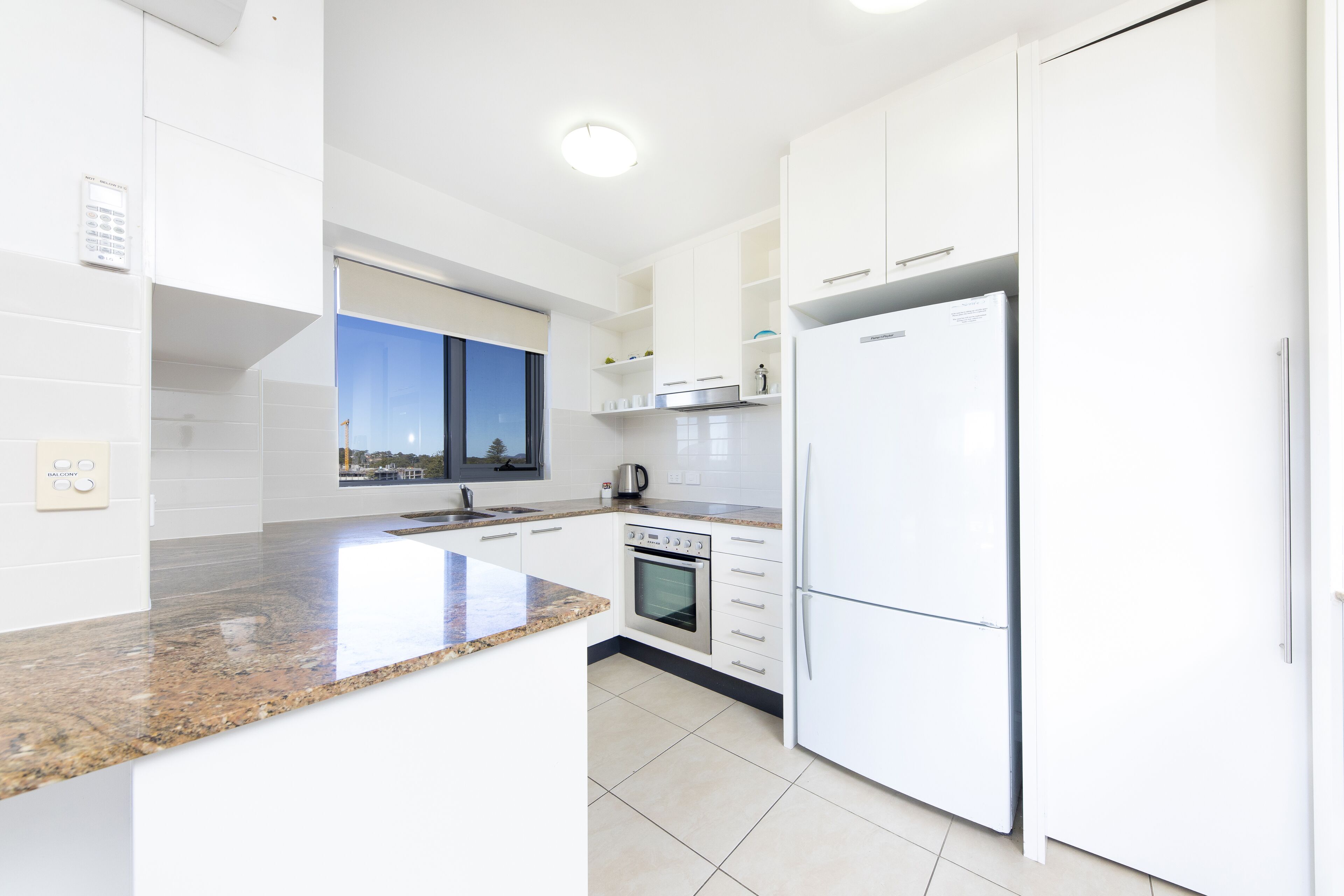 A modern kitchen with white cabinetry, a granite countertop, a built-in oven, and a refrigerator.