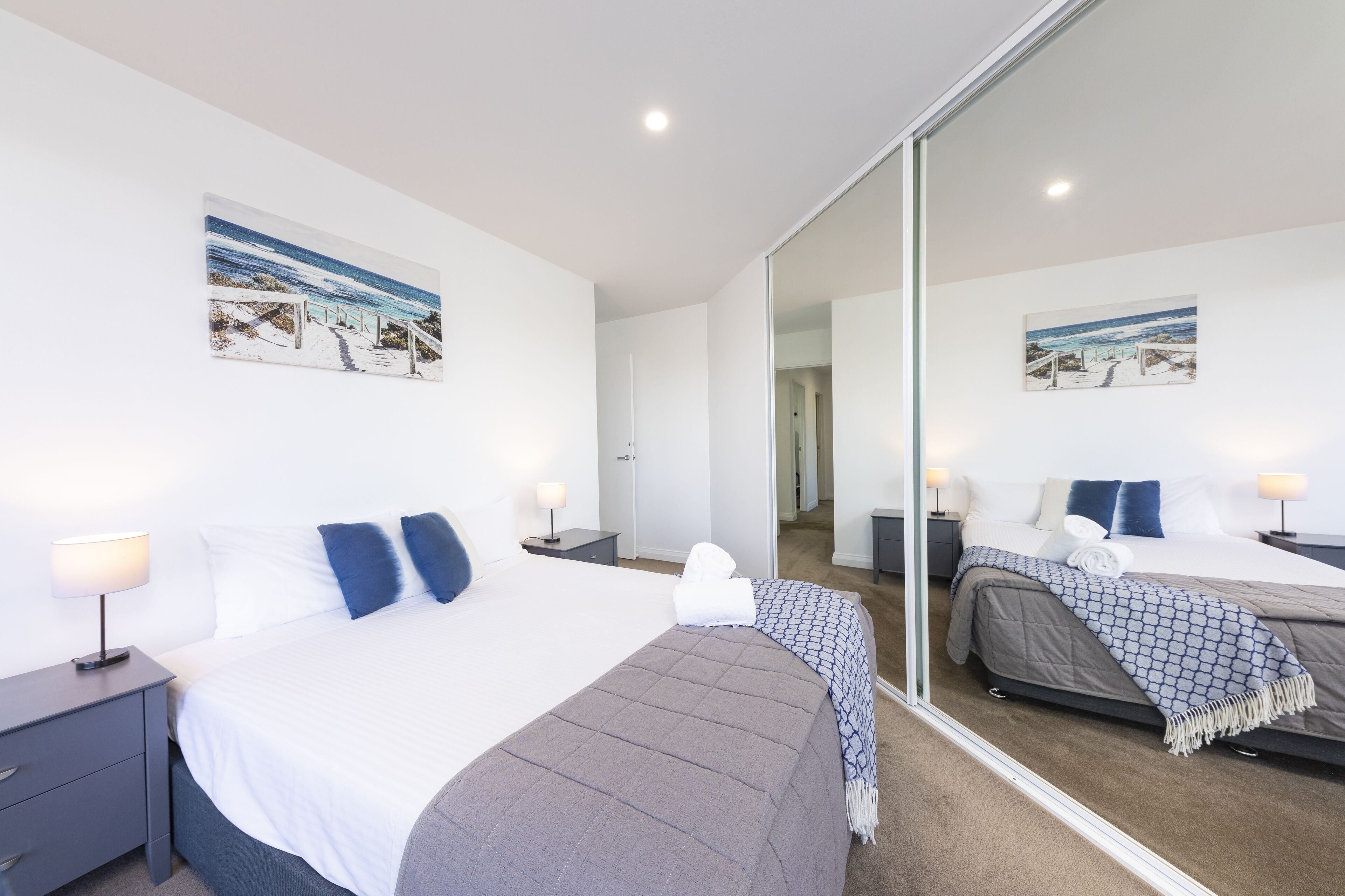 A modern hotel room with a large bed, a bedside table, a nightstand, and a mirror.