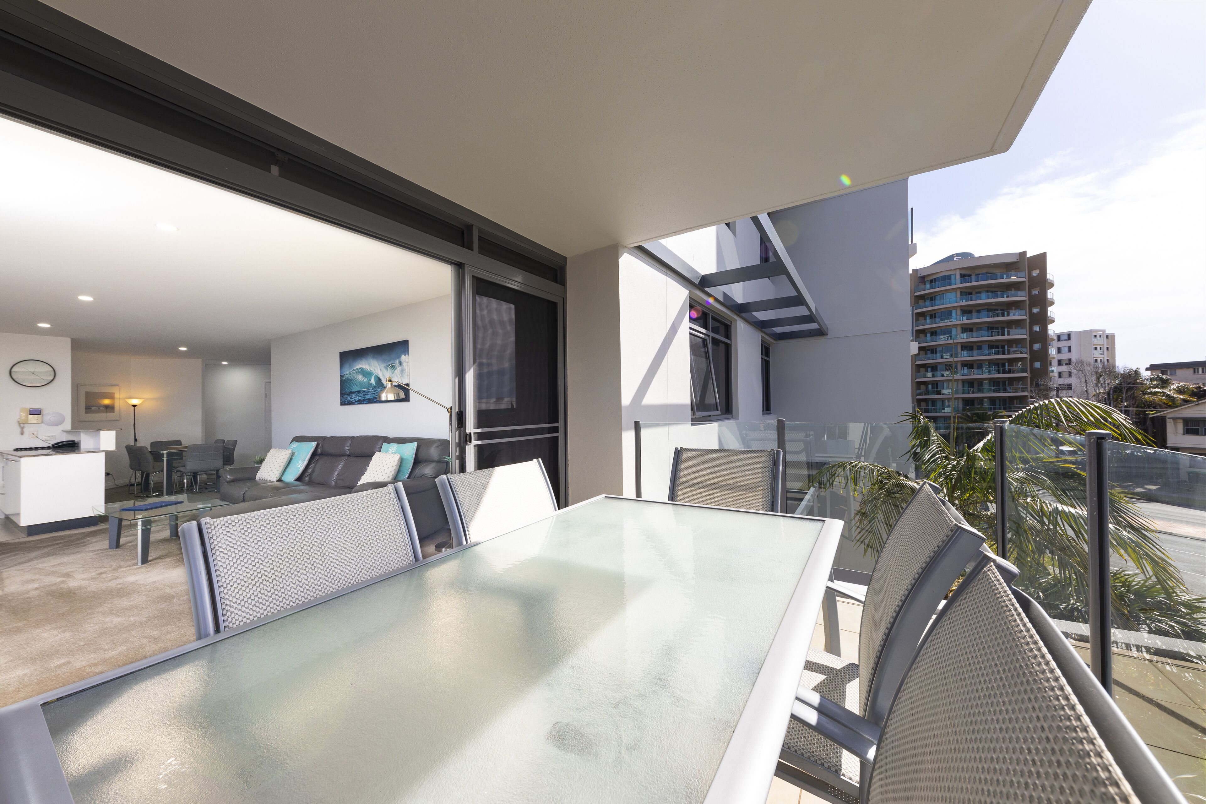 A modern living room with a glass table and chairs, a sofa, and a dining area.