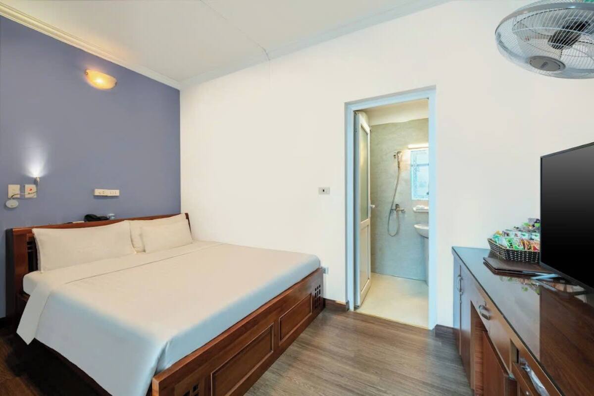 Habitación de hotel con cama, televisor, escritorio y baño visible a través de una puerta abierta.