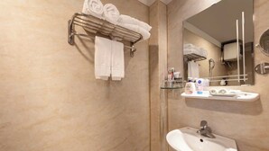A bathroom with a marble wall, a sink, a mirror, and a towel rack with folded towels. - A25 Hotel - Doi Can 2 (Hanoi)