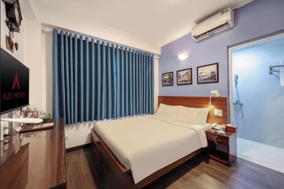 Una habitación de hotel con cama, escritorio con televisor, mesita de noche y ducha.