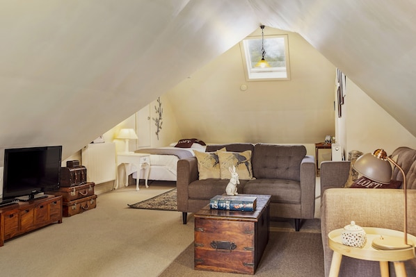 A cozy loft-style living room with a television, a sofa, a coffee table, and a bookshelf.