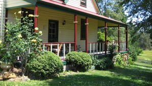Uma casa de dois andares com varanda, telhado vermelho e jardim com arbustos e flores.