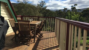 Um deck de madeira com mesa, cadeiras, churrasqueira e vista para uma área arborizada.