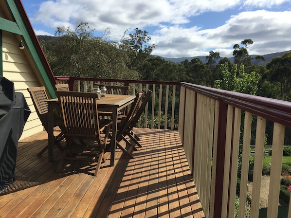 A wooden deck with a table and chairs, a barbecue grill, and a view of a forested area.