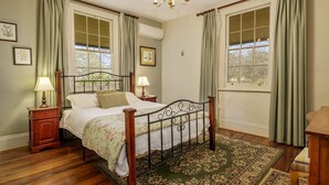 Um quarto com cama de dossel, duas mesas de cabeceira com abajures, um lustre e uma janela grande com cortinas.