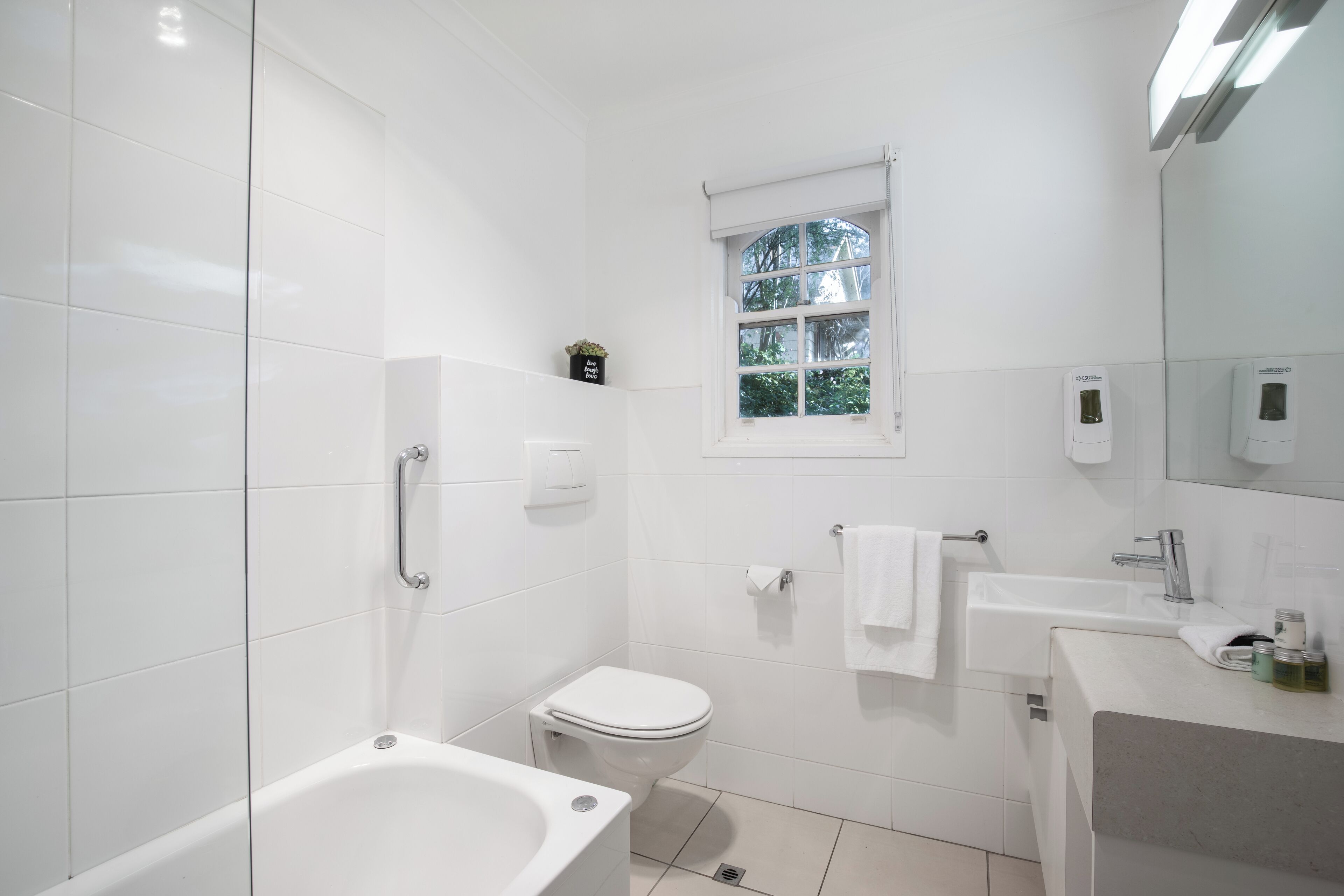 Ein modernes Badezimmer mit Badewanne, Toilette, Waschbecken und einem Fenster.