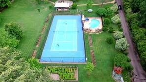 Vista aérea de una cancha de tenis rodeada de céspedes cuidados y una piscina.