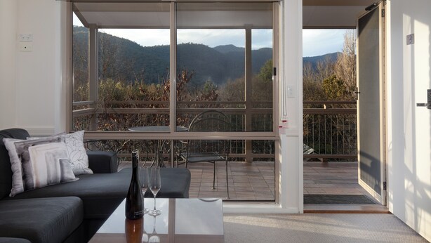 Una sala de estar moderna con un sofá, una mesa de centro y vistas a un balcón con un paisaje montañoso.