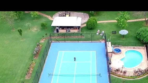 An aerial view of a tennis court surrounded by a fence, with a pool and a sign reading "Chestnut Tree" in the foreground. - Chestnut Tree Holiday Apartments (Bright)