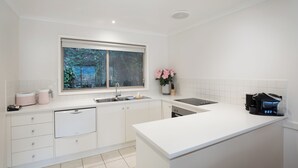 Cocina moderna con armarios blancos, horno empotrado, lavabo y ventana con vistas a zonas verdes.