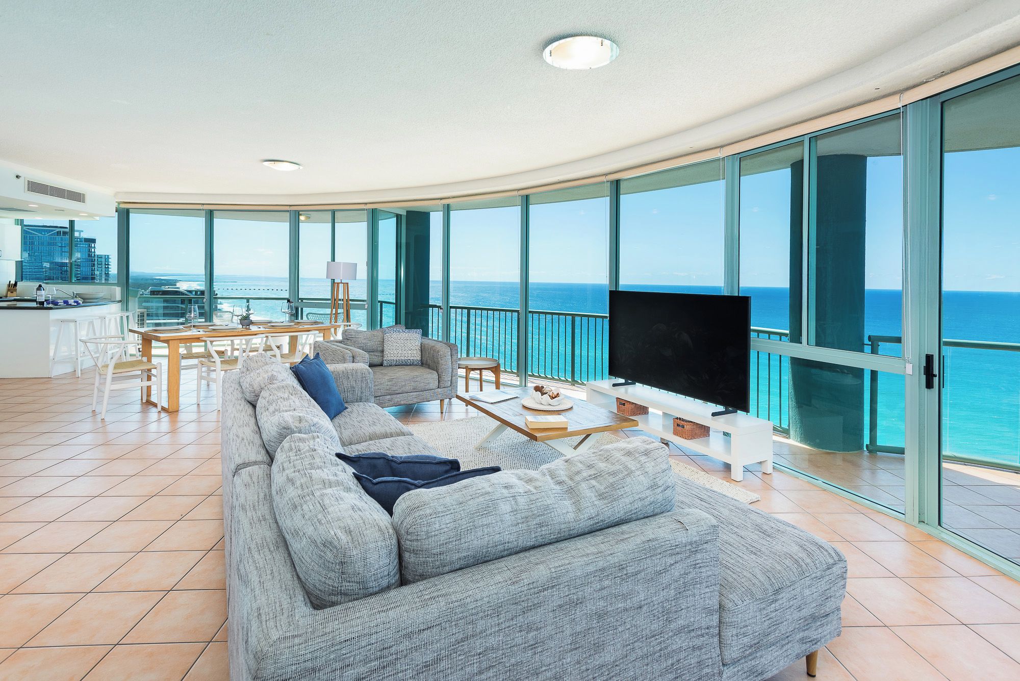 A spacious living area with a large gray sofa, a flat-screen TV, and a dining table.