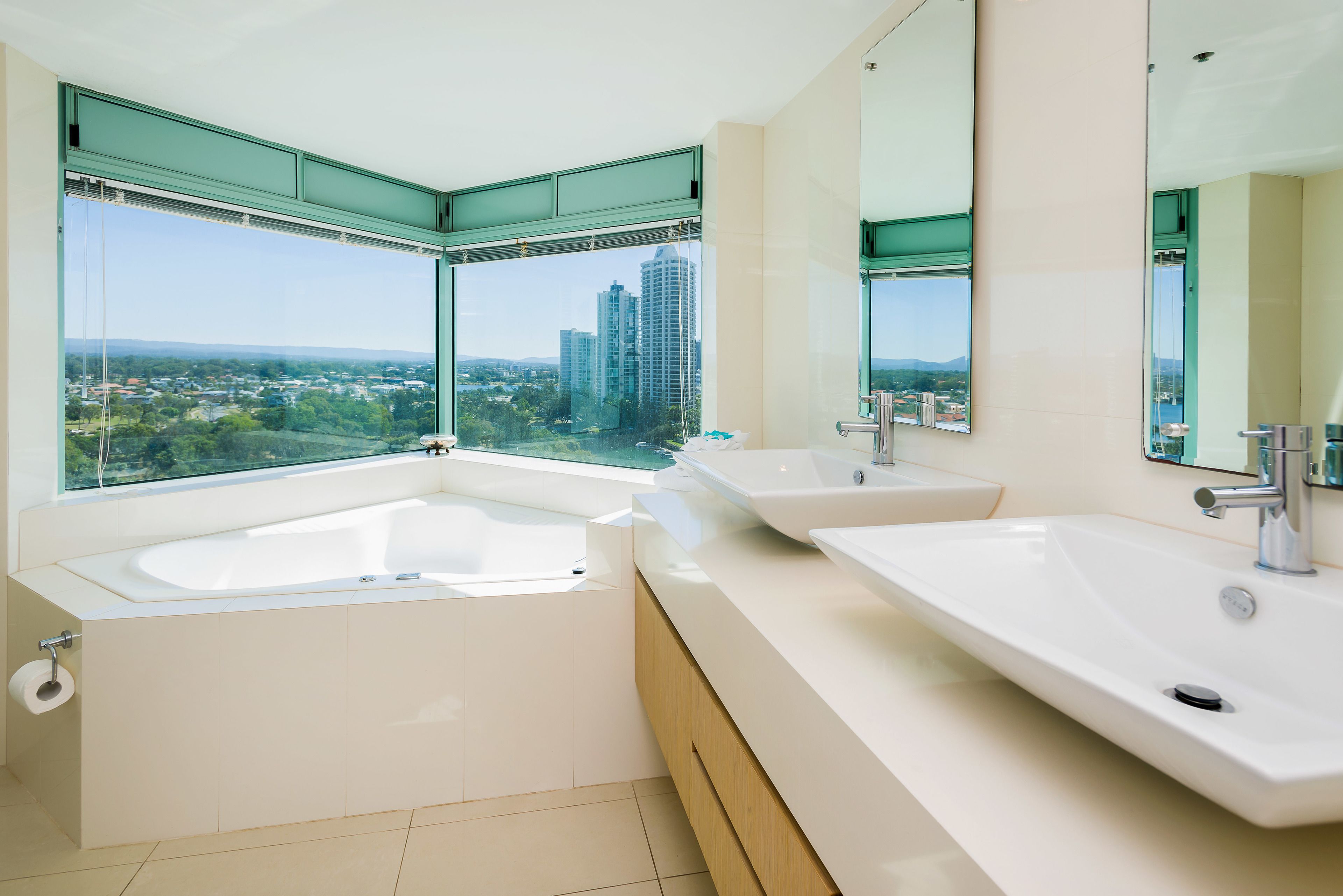 A modern bathroom with a large bathtub, two sinks, and a large window offering a city view.
